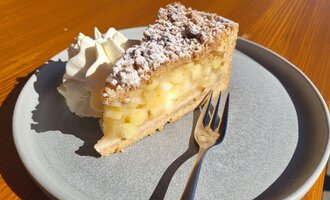 Ein Stück Apfelkuchen auf einem Teller, garniert mit Sahne. Der Kuchen hat eine knusprige Kruste und ist mit Apfelstücken gefüllt.