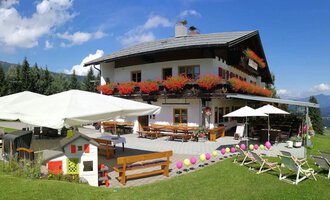 Ein gemütliches Haus in den Bergen mit bunten Blumenkästen und Terrassen mit Sonnenschirmen. Die Umgebung ist grün und bietet einen schönen Ausblick auf die Landschaft. | © Cafe Walserblick | Marcus Dornach