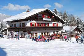 Ein traditionelles Chalet im Schnee mit roten Fensterläden. Viele Menschen genießen die Winteraktivitäten rund um das Gebäude.