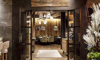 An inviting entrance to a restaurant with wooden details and warm lighting. The atmosphere is cozy and welcoming. | © A-ROSA Ifen Hotel Kleinwalsertal