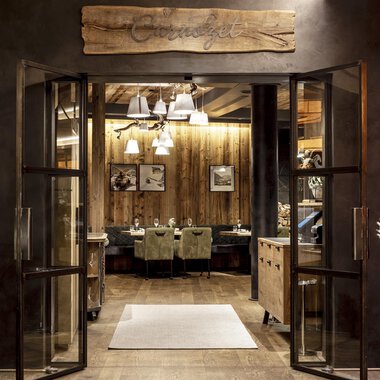 An inviting entrance to a restaurant with wooden details and warm lighting. The atmosphere is cozy and welcoming. | © A-ROSA Ifen Hotel Kleinwalsertal