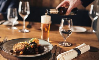 A set table with a plate of delicious food and a glass of beer. An elegant atmosphere with wine and water glasses. | © A-ROSA Ifen Hotel Kleinwalsertal