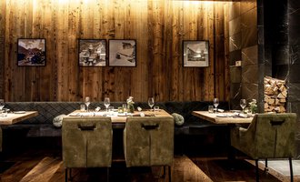 A modern restaurant with wooden walls and stylish furniture. The tables are elegantly set, and pictures hang on the wall. | © A-ROSA Ifen Hotel Kleinwalsertal
