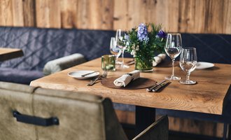 A beautifully set table in a cozy restaurant. The wooden surface is decorated with glasses, dishes, and a flower. | © A-ROSA Ifen Hotel Kleinwalsertal
