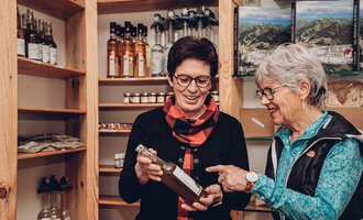 Two women are looking at a bottle together in a store. Shelves with additional products can be seen in the background. | © Carolin Ries | www.calejofotografie.de