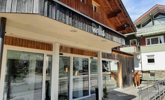Ein modernes Gebäude mit Holzverkleidung steht im Vordergrund. Es gibt große Fenster und eine entspannte Atmosphäre in der Umgebung. | © das Wallis Restaurant & Brasserie | Veronika Senn