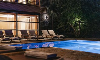 Ein eleganter Poolbereich mit Liegen und sanfter Beleuchtung. Der Pool spiegelt das Licht der Umgebung wider und schafft eine entspannte Atmosphäre. | © Naturhotel Chesa Valisa