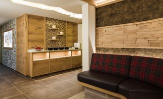 Ein moderner Empfangsbereich mit Holzverkleidung und gemütlicher Sitzgelegenheit. Die Atmosphäre ist warm und einladend. | © Hotel Leitner