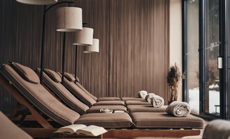 A relaxing wellness area with comfortable loungers and soft lighting. Large windows offer a view of nature. | © A-ROSA Ifen Hotel Kleinwalsertal