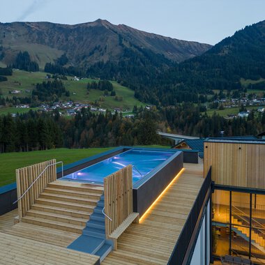 A modern terrace with a pool and wooden flooring, surrounded by picturesque mountains. The view of the landscape is stunning and conveys a sense of tranquility. | © Genuss- & Aktivhotel Sonnenburg |Heike Wohlgenannt
