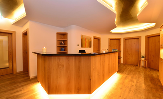 A modern reception area with a wooden counter and soft lighting. The walls are kept neutral, creating an inviting atmosphere. | © Hotel Alpenstüble KG
