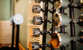 Eine Reihe von Hanteln in einem Fitnessstudio. Der Hintergrund ist unscharf und zeigt Texturen der Wände. | © Hotel Alpenstüble KG