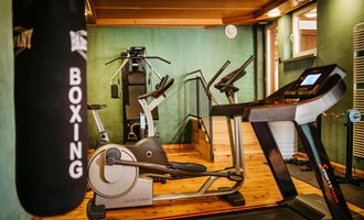 Ein modernes Fitnessstudio mit verschiedenen Trainingsgeräten. Im Vordergrund sind ein Laufband und ein Boxsack zu sehen. | © Hotel Alpenstüble KG