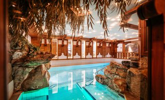 An elegant indoor pool with clear water and rocks in the background. The wooden paneling and soft lighting create a relaxed atmosphere. | © Hotel Alpenstüble KG