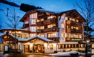 A cozy hotel in the mountains at night. The facade is illuminated and surrounded by snow-covered trees. | © Hotel Alpenstüble KG