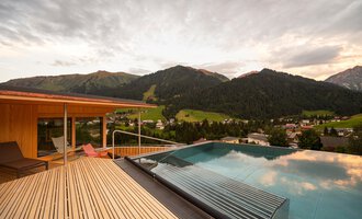 A beautiful view of the mountains from a terrace with an infinity pool. The clouds in the sky give the scene a relaxed atmosphere.