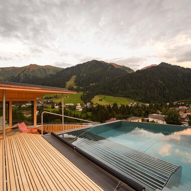A beautiful view of the mountains from a terrace with an infinity pool. The clouds in the sky give the scene a relaxed atmosphere.