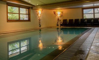A beautiful indoor pool with illuminated walls and relaxing loungers. The water reflects the surroundings and creates a tranquil atmosphere. | © IFA Hotel Alpenhof Wildental | Andreas Froschauer
