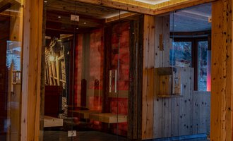 Ein moderner Empfangsbereich mit Holzelementen und großen Glasflächen. Die gemütliche Atmosphäre wird durch warmes Licht und geschmackvolle Dekorationen verstärkt. | © IFA Hotel Alpenhof Wildental | Andreas Froschauer
