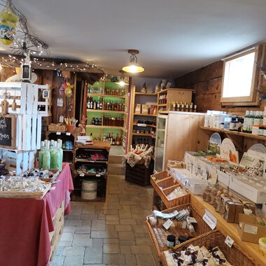 Ein gemütlicher Laden mit Holzwänden, der verschiedene Produkte wie Geschenke und lokale Lebensmittel anbietet. Das Ambiente ist einladend und freundlich. | © Dies & Das Hofladen | V. Wächter