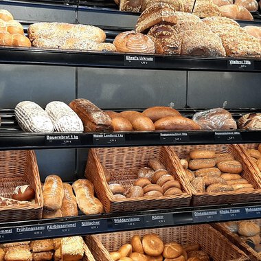 Ein Regal voller frischer Brötchen und Brote in verschiedenen Formen. Die Auswahl reicht von Körnerbrötchen bis zu klassischen Broten. | © Ehrat´s Backmanufaktur | Veronika Senn