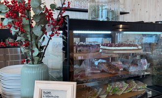 Ein einladender Cafébereich mit einer Glasvitrine voller Gebäck und Snacks. Neben der Vitrine steht eine Vase mit roten Beeren. | © Einkehr Guntschau