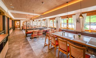 Ein modernes Restaurant mit Holzmöbeln und einer einladenden Atmosphäre. Große Fenster lassen viel Tageslicht herein und bieten einen Blick ins Freie. | © Familienhotel Kleinwalsertal Hotelgesellschaft mbH