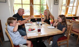 Eine Familie genießt ihr Essen und Eis in einem gemütlichen Restaurant. Sie lachen und haben Spaß am Tisch. | © Familienhotel Kleinwalsertal Hotelgesellschaft mbH