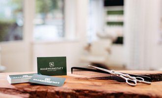 Ein Friseursalon mit einer Holzoberfläche und Haarschneideutensilien. Auf dem Tisch liegen Visitenkarten mit dem Namen "HAARWERKSTATT". | © Friseur Haarwerkstatt | Franziska Diener