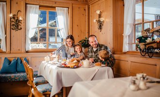 A family enjoys breakfast in a cozy wooden house. On the table are various breakfast dishes and a friendly atmosphere. | © Hotel Alpenstüble KG