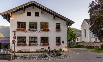 Ein charmantes Gemeindegebäude mit blühenden Blumenkästen. Im Hintergrund sind weitere Gebäude und Bäume zu sehen. | © Kleinwalsertal Tourismus |  Steffen Berschin