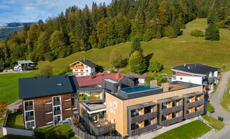 A modern building in the greenery, surrounded by trees and hills. The architecture combines wood and glass, creating an inviting atmosphere.
