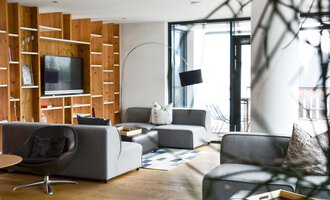 A modern living room with gray sofas and a large television. Large windows provide plenty of light and an open space. | © Katharina Wohlgenannt