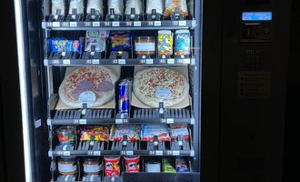 Ein Snackautomat mit verschiedenen Getränken und Lebensmitteln. Darunter befinden sich Pizzen, Süßigkeiten und Energydrinks. | © Gerd am Herd | Gerd Hammerer