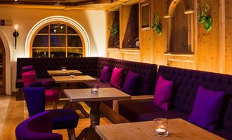 Ein einladendes Restaurant mit gemütlichen Sitzecken und warmem Holzinterieur. Die lila Kissen auf den Bänken schaffen eine entspannte Atmosphäre. | © Haller's Geniesserhotel | Dietmar Walser