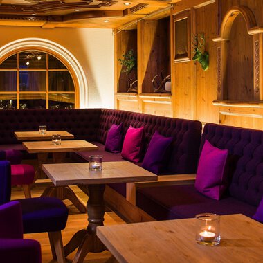 Ein einladendes Restaurant mit gemütlichen Sitzecken und warmem Holzinterieur. Die lila Kissen auf den Bänken schaffen eine entspannte Atmosphäre. | © Haller's Geniesserhotel | Dietmar Walser