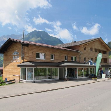 A modern wooden building in a picturesque mountain landscape. The clear skies and surrounding mountains give the place an inviting character. | © Sport Hilbrand GmbH