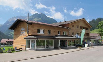 A modern wooden building in the mountains. Surrounded by a beautiful landscape with green forests and mountains. | © Sport Hilbrand GmbH