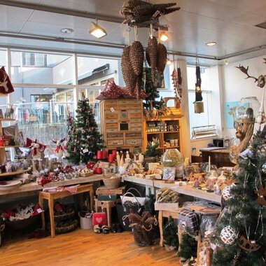 Ein einladender Geschenkeladen mit festlicher Dekoration. Überall sind Weihnachtsbäume und liebevoll gestaltete Produkte zu sehen. | © HUIMWEA Alpendekor