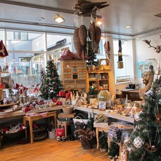 Ein einladender Geschenkeladen mit festlicher Dekoration. Überall sind Weihnachtsbäume und liebevoll gestaltete Produkte zu sehen. | © HUIMWEA Alpendekor