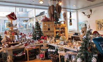 Ein einladender Geschenkeladen mit festlicher Dekoration. Überall sind Weihnachtsbäume und liebevoll gestaltete Produkte zu sehen. | © HUIMWEA Alpendekor
