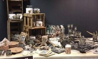Ein stilvoller Tisch mit Holzdeko und verschiedenen Glasbehältern. Auf dem Tisch sind auch Bilderrahmen und kleine Naturaccessoires arrangiert. | © HUIMWEA Alpendekor