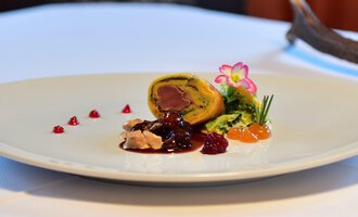 Ein kunstvoll angerichtetes Gericht auf einem weißen Teller. Es enthält eine Füllung mit Fleisch, begleitet von verschiedenen Saucen und Garnituren. | © Alpenhof Jäger | Werbewind