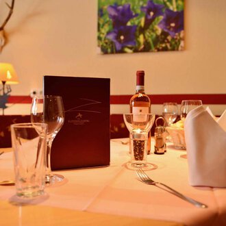Ein schön gedeckter Tisch in einem eleganten Restaurant. Auf dem Tisch stehen Gläser, ein Weinflasche und eine Menükarte. | © IFA Breitach Apartements
