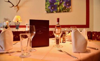Ein schön gedeckter Tisch in einem eleganten Restaurant. Auf dem Tisch stehen Gläser, ein Weinflasche und eine Menükarte. | © IFA Breitach Apartements