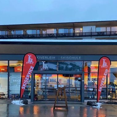 Ein modernes Skizentrum mit großen Fenstern und rot-weißen Fahnen. Der Eingangsbereich ist einladend und spiegeln die winterliche Atmosphäre wider. | © Ifensport | Thomas MARTIN