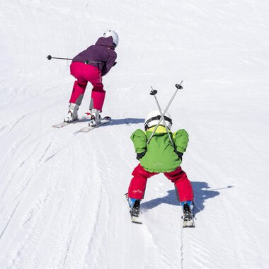 Zwei Kinder fahren Ski auf einer verschneiten Piste. Das eine Kind trägt eine grüne Jacke und das andere eine lila Jacke. | © Kleinwalsertal Tourismus | Dominik Berchtold
