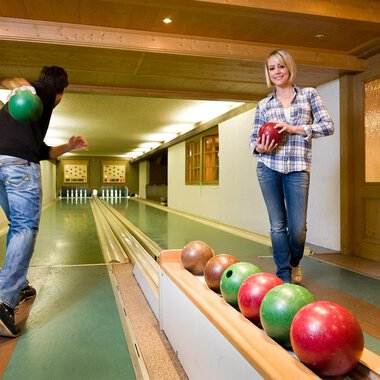 A cozy bowling alley with two people playing. One person throws a ball while the other stands on the lane holding a ball in hand. | © Aparthotel Kleinwalsertal Haller GmbH & Co KG