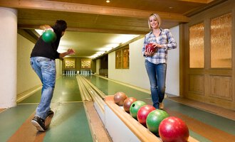 A cozy bowling alley with two people playing. One person throws a ball while the other stands on the lane holding a ball in hand. | © Aparthotel Kleinwalsertal Haller GmbH & Co KG