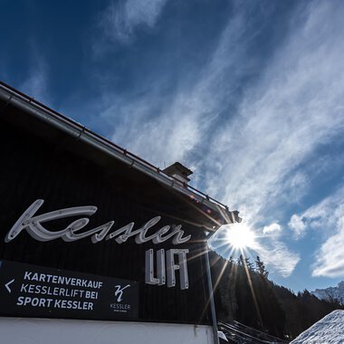 A clearly visible sign with the name "Kessler" on a foreground building. In the background, the sky and the mountains are visible. | © Sport Kessler GmbH